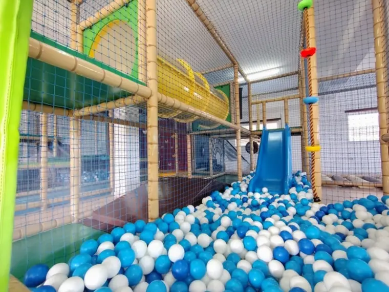 Piscina de bolas com escorrega azul e presas de escalada na estrutura